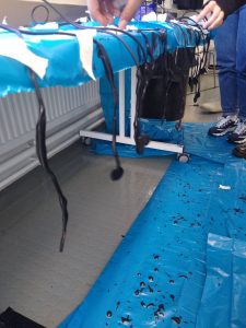 microphones handing off a table covered in blue plastic, with drips of black below on the floor that is also covered in blue plastic