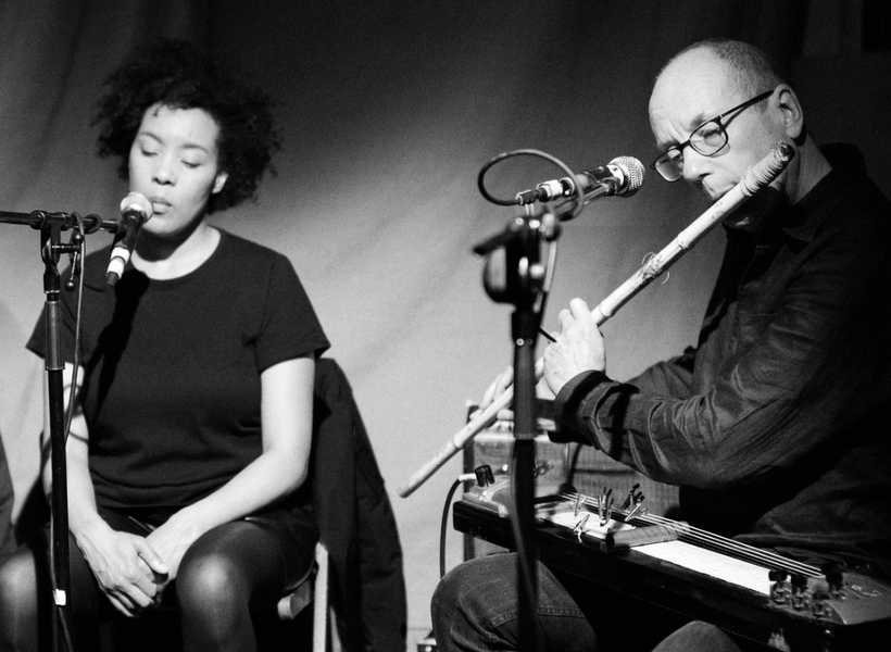 A woman singing into a microphone and a man playing an instrument into a microphone