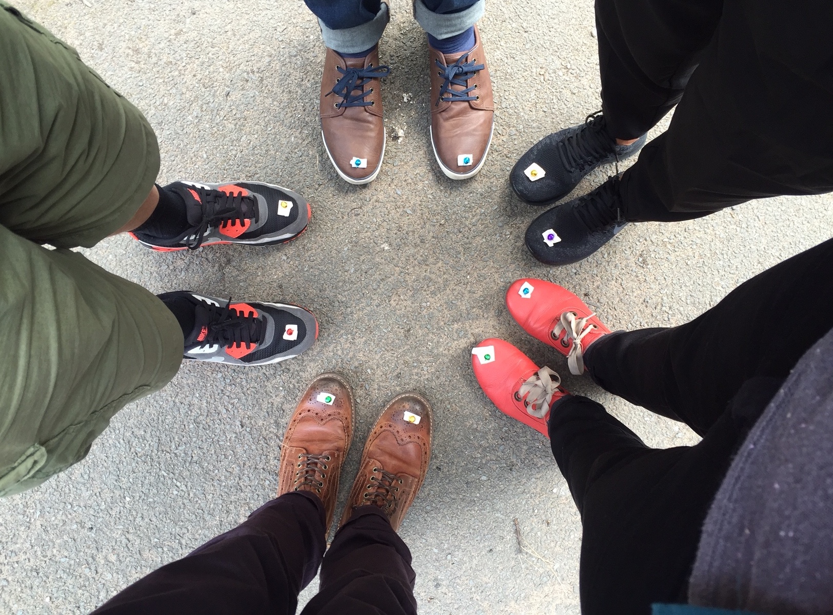 five peoples lower legs and feet, stood in a circle, with stickers on their shoes