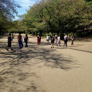 15+ people walking across a large tarmac area towards trees