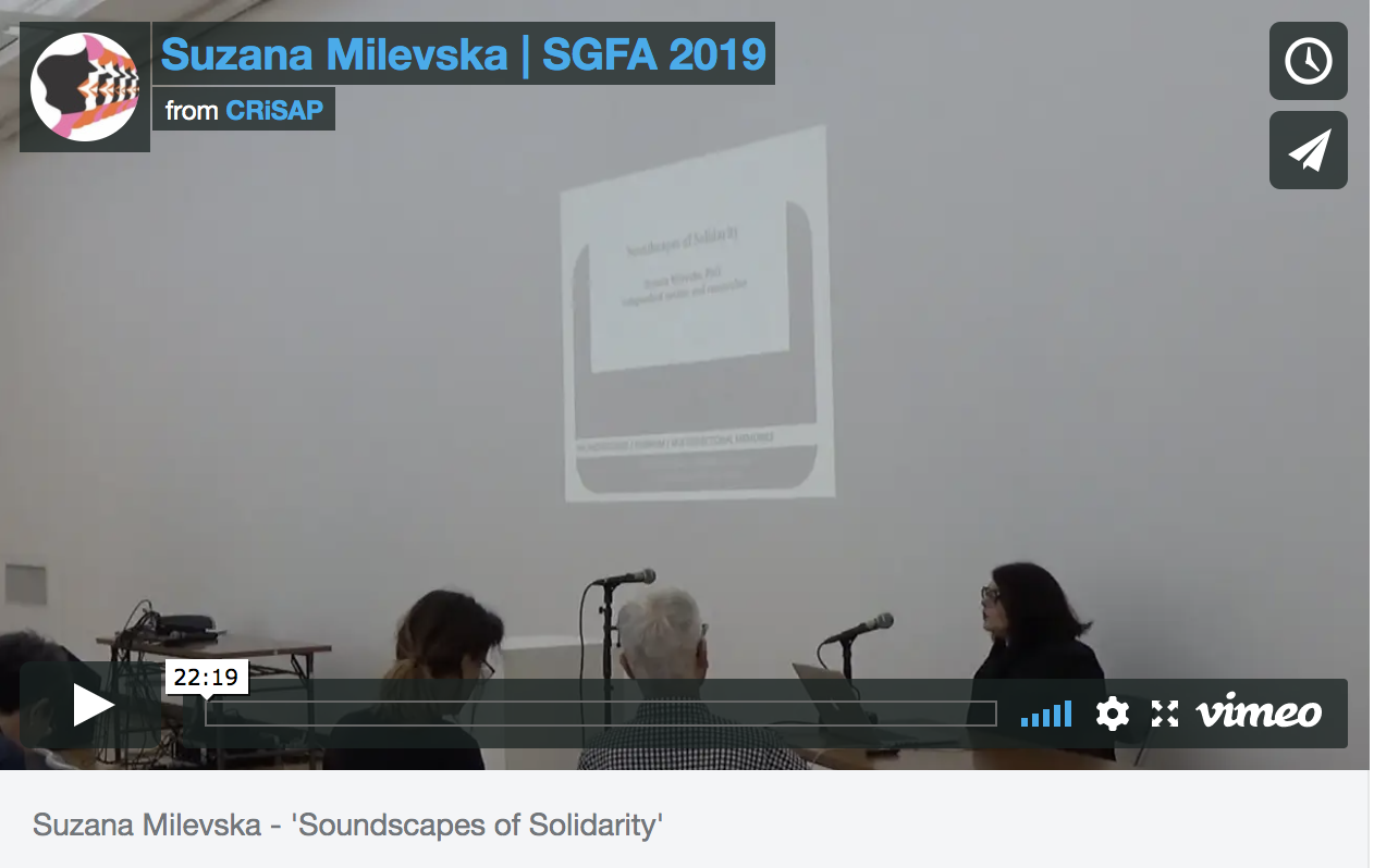 a vimeo still of a video showing a woman talking into a microphone by a projection. Text reads "Suzana Milveska | SGFA 2019, from CRiSAP"