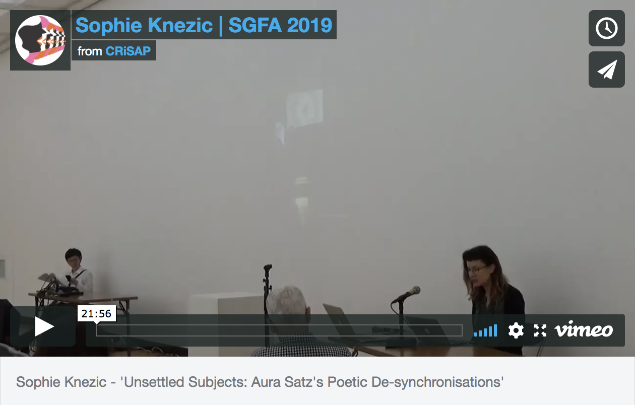 a vimeo still of a video showing a woman talking into a microphone by a projection. Text reads "Sophie Knezic | SGFA 2019, from CRiSAP"