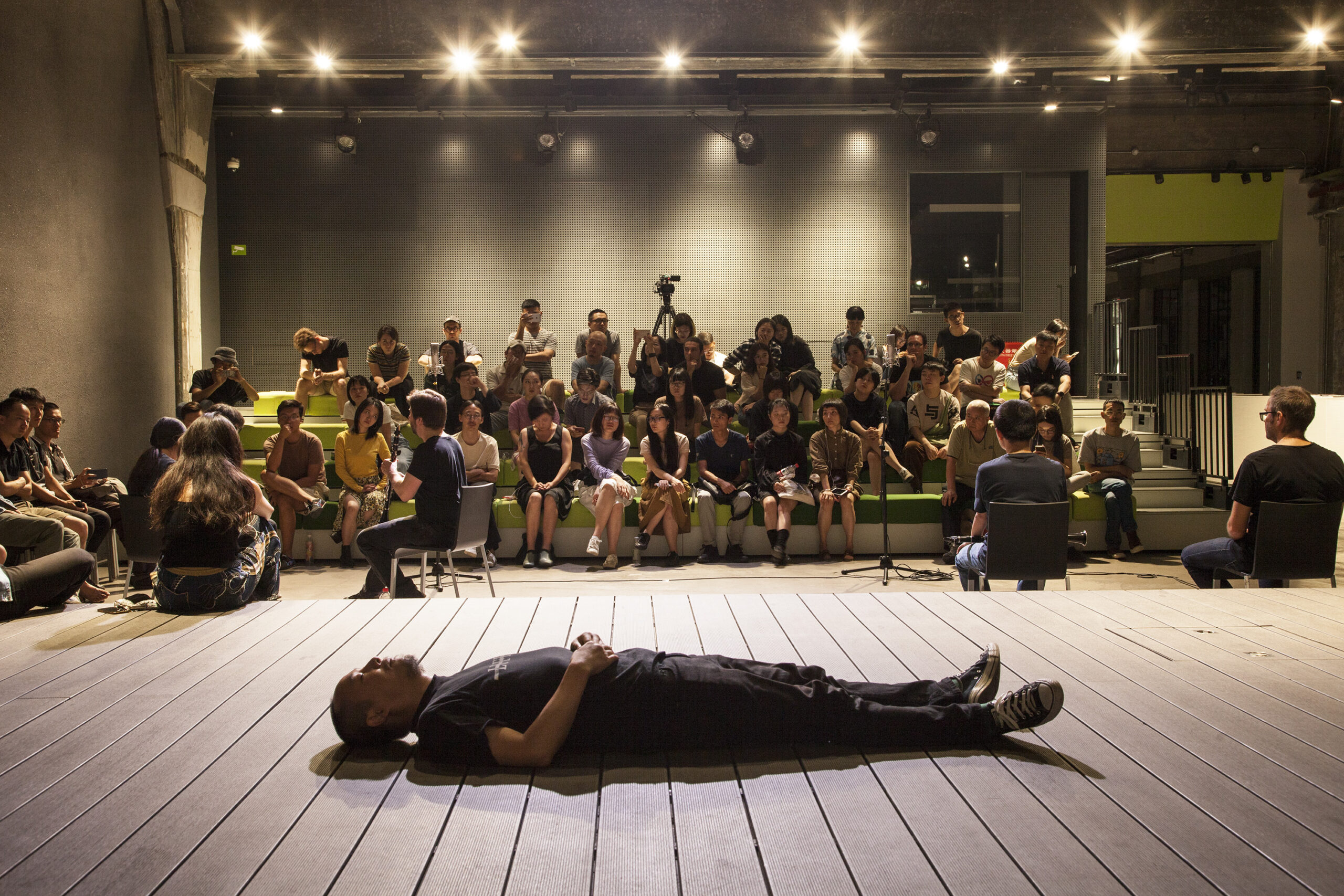 Profile image of Yan Jun lying on a stage in front of an audience
