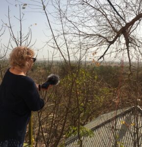 Cathy holding a recording device towards an outdoor landscape