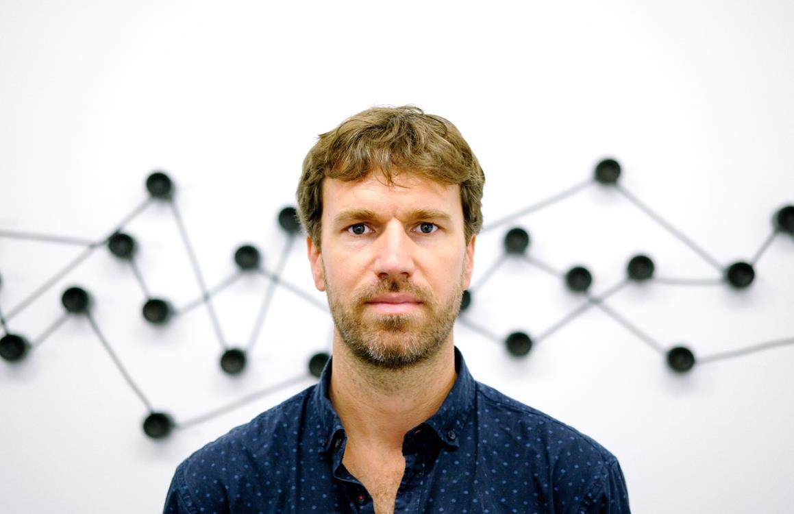 Profile image of Felix Blume looking directly at the camera, standing in an art gallery with speakers behind