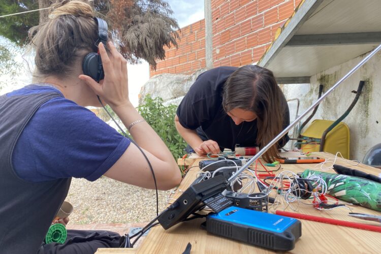 Brigitte and Lisa making and listening to radios, outdoors at a table full of equipment