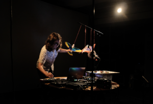 Kate performing at a desk with mixed electronics and plastic birds