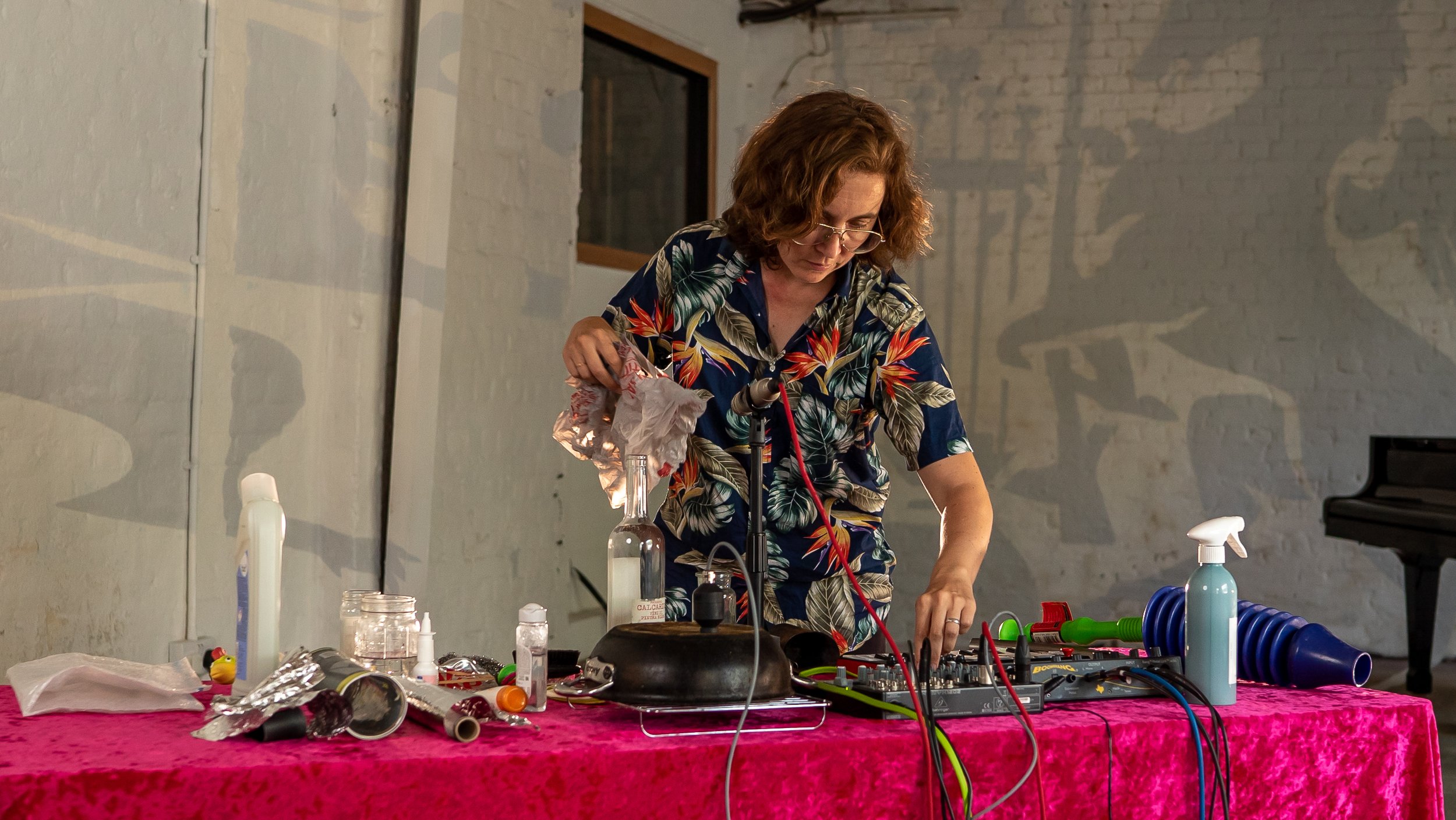 Kate Carr performing 'rubbish music' - at a table with electronics and household items